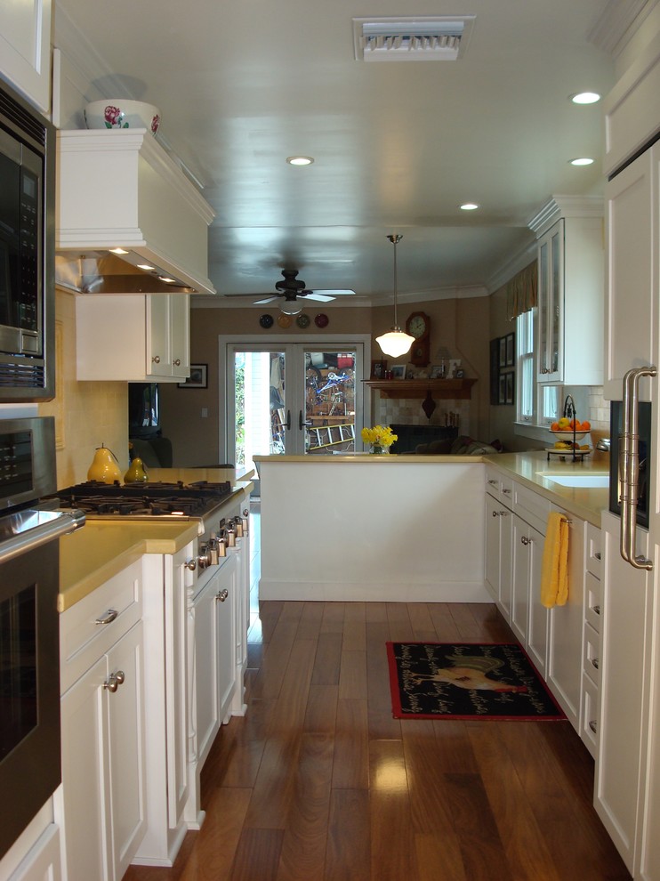 Exempel på ett avskilt, mellanstort eklektiskt l-kök, med en undermonterad diskho, luckor med upphöjd panel, vita skåp, bänkskiva i kvarts, gult stänkskydd, rostfria vitvaror, mellanmörkt trägolv och stänkskydd i keramik