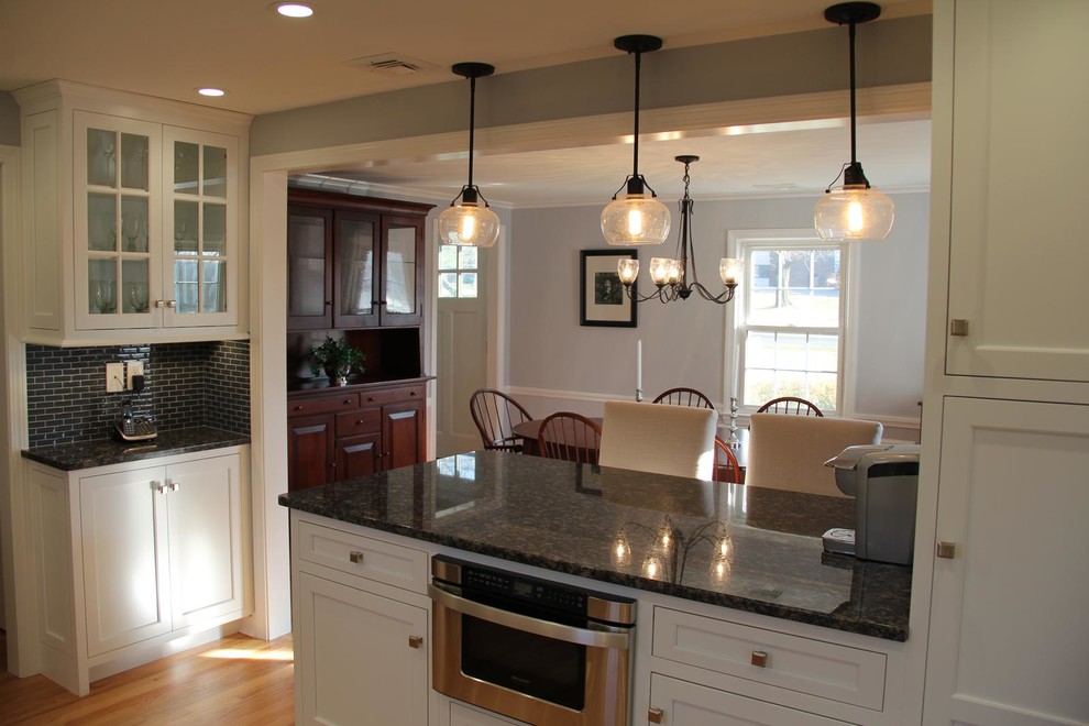 Klassisk inredning av ett avskilt l-kök, med en nedsänkt diskho, luckor med infälld panel, vita skåp, granitbänkskiva, grått stänkskydd, stänkskydd i tunnelbanekakel, rostfria vitvaror, ljust trägolv och en köksö