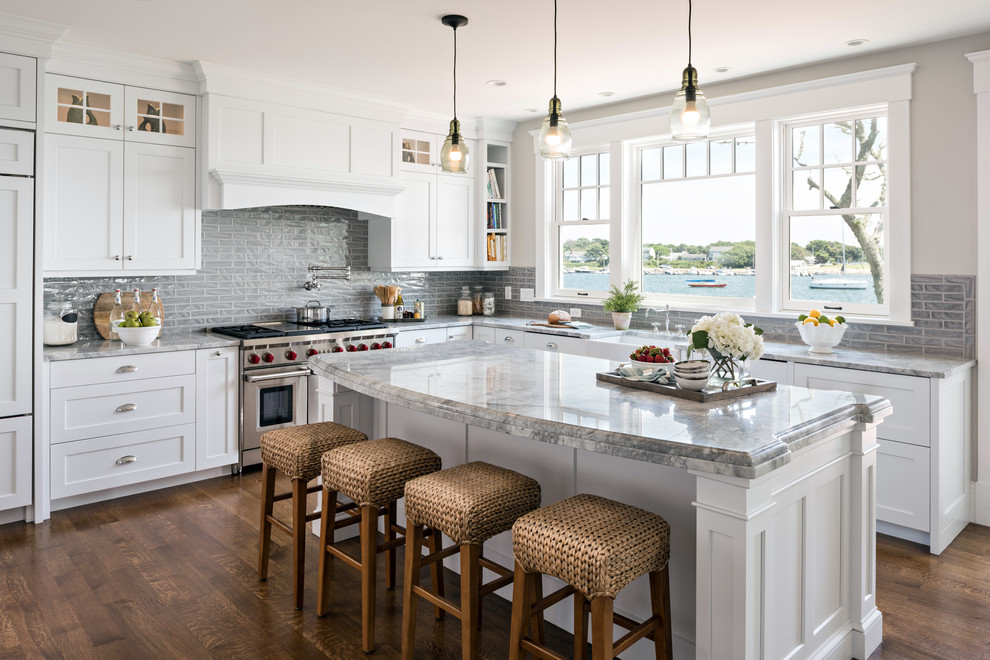This is an example of a beach style kitchen in Boston with a belfast sink, shaker cabinets, white cabinets, quartz worktops, grey splashback, porcelain splashback, stainless steel appliances, medium hardwood flooring, an island and brown floors.
