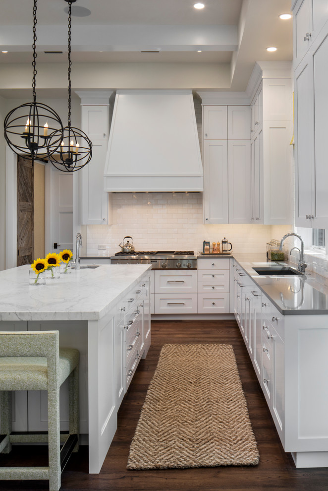 Beach style l-shaped dark wood floor and brown floor kitchen photo in Jacksonville with an undermount sink, white cabinets, white backsplash, subway tile backsplash, stainless steel appliances, an island and recessed-panel cabinets