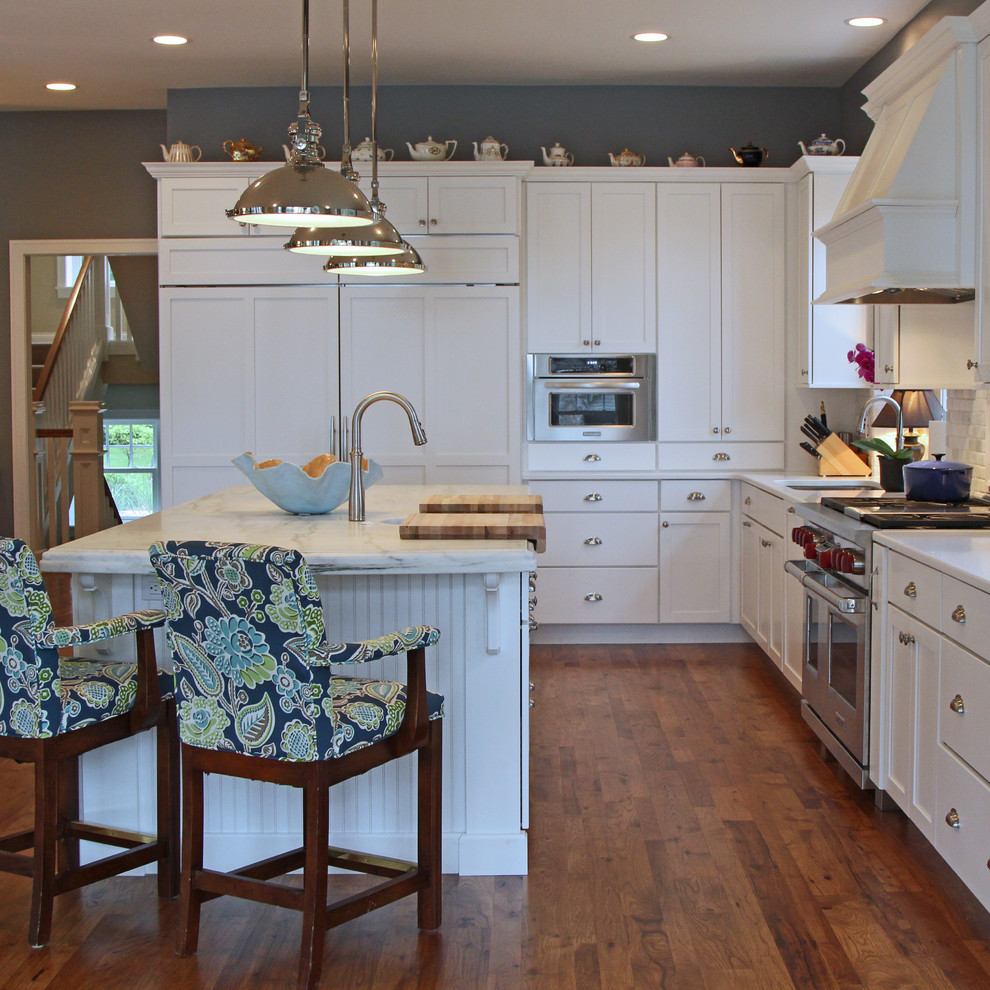 Inspiration for a large timeless l-shaped medium tone wood floor eat-in kitchen remodel in Milwaukee with a single-bowl sink, recessed-panel cabinets, white cabinets, marble countertops, stone tile backsplash, paneled appliances and two islands