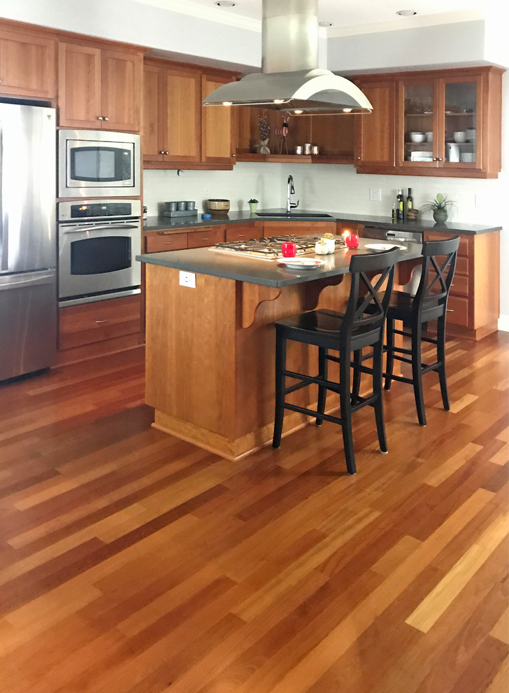 Amerikansk inredning av ett litet grå grått kök, med en undermonterad diskho, skåp i shakerstil, skåp i mellenmörkt trä, bänkskiva i kvarts, vitt stänkskydd, stänkskydd i keramik, rostfria vitvaror, mellanmörkt trägolv, en köksö och brunt golv