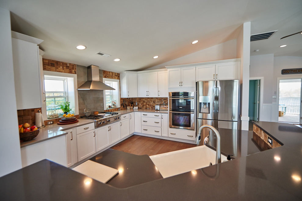 Mid-sized trendy l-shaped medium tone wood floor and brown floor open concept kitchen photo in Other with a farmhouse sink, shaker cabinets, white cabinets, solid surface countertops, brown backsplash, wood backsplash, stainless steel appliances, an island and gray countertops