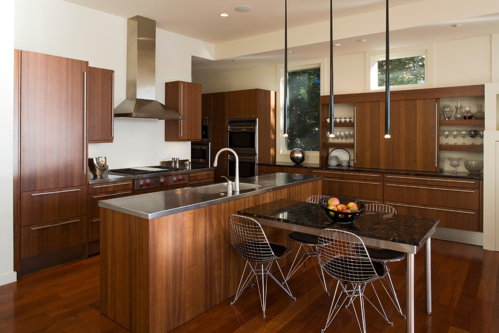 Modelo de cocina comedor contemporánea con fregadero integrado, armarios con paneles lisos, puertas de armario de madera en tonos medios y encimera de acero inoxidable