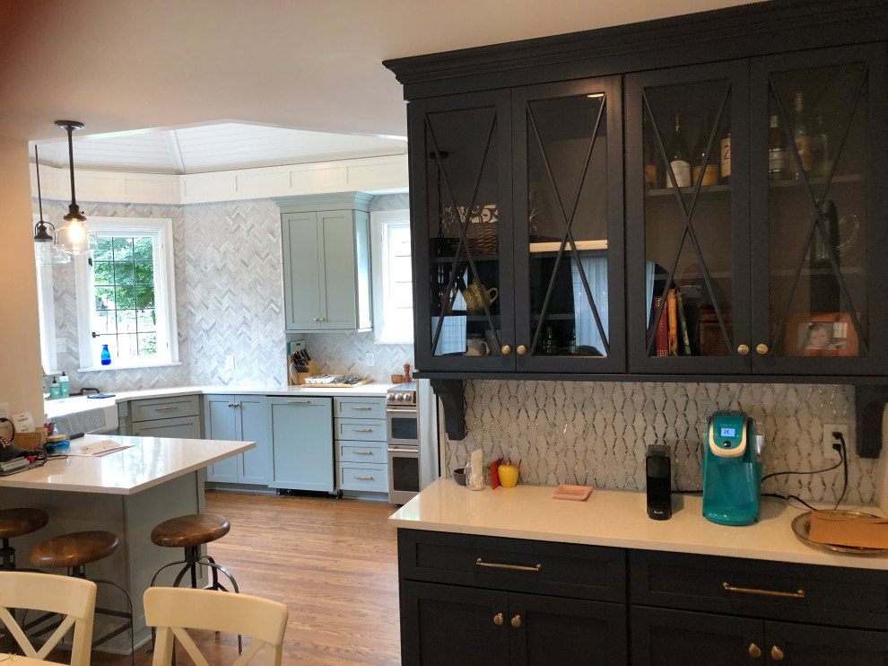 Cette image montre une cuisine américaine traditionnelle de taille moyenne avec un évier de ferme, des portes de placard bleues, une crédence grise, un électroménager en acier inoxydable, un sol en bois brun, un sol marron et un plafond décaissé.
