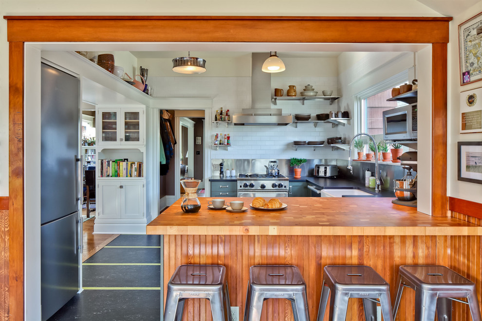 Klassische Küche in U-Form mit Landhausspüle, Arbeitsplatte aus Holz, Küchengeräten aus Edelstahl, offenen Schränken, Küchenrückwand in Weiß, Rückwand aus Metrofliesen, grünen Schränken und schwarzem Boden in Seattle