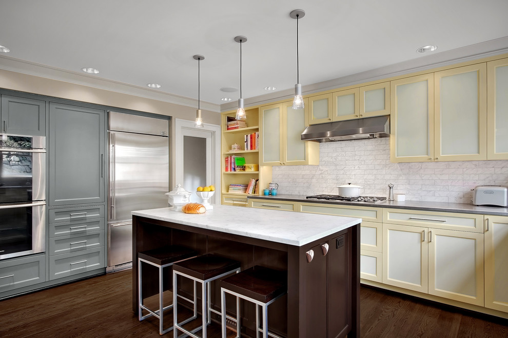 Modern inredning av ett kök, med rostfria vitvaror, luckor med infälld panel, gula skåp, bänkskiva i rostfritt stål, vitt stänkskydd och stänkskydd i stenkakel