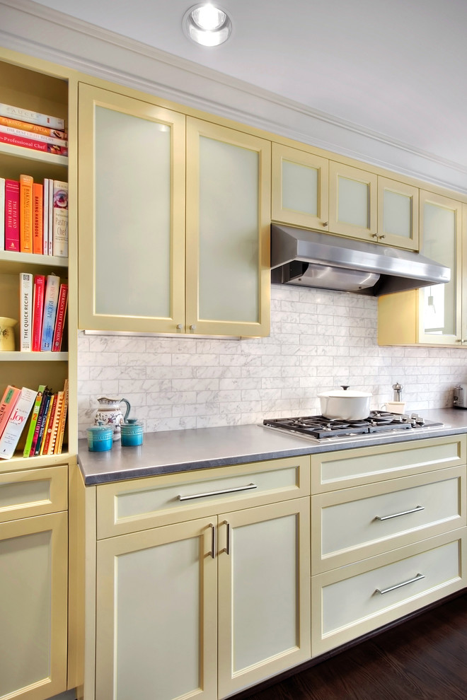 Foto di una cucina minimal con elettrodomestici in acciaio inossidabile, ante con riquadro incassato, ante gialle, top in acciaio inossidabile, paraspruzzi bianco e paraspruzzi in marmo
