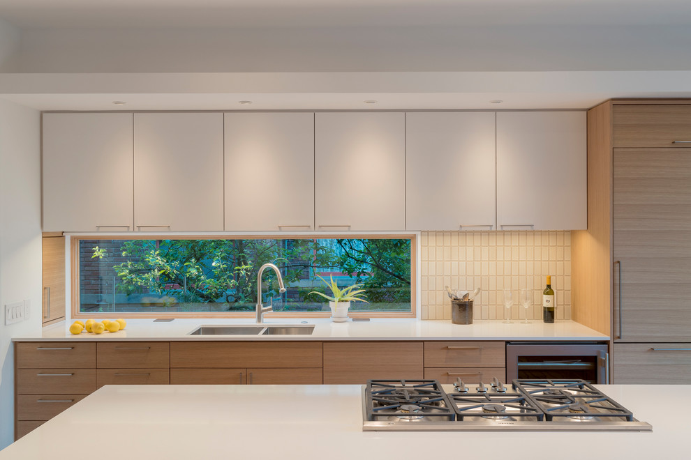 Design ideas for a medium sized modern galley open plan kitchen in Seattle with a submerged sink, flat-panel cabinets, light wood cabinets, engineered stone countertops, beige splashback, ceramic splashback, stainless steel appliances, light hardwood flooring and an island.
