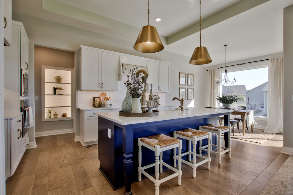 Eat-in kitchen - transitional l-shaped medium tone wood floor and brown floor eat-in kitchen idea in Wichita with a farmhouse sink, white cabinets, granite countertops, white backsplash, subway tile backsplash, stainless steel appliances, an island and shaker cabinets