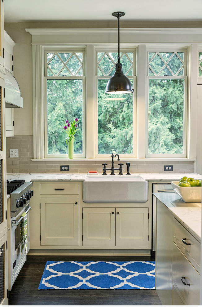 Example of a mid-sized classic u-shaped dark wood floor eat-in kitchen design in Portland with a farmhouse sink, white cabinets, beige backsplash, ceramic backsplash, stainless steel appliances, marble countertops, recessed-panel cabinets and an island