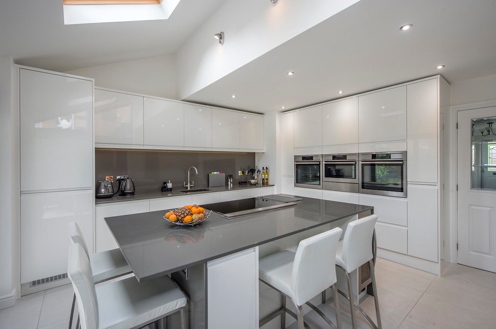 This is an example of a large l-shaped kitchen/diner in Other with a submerged sink, flat-panel cabinets, white cabinets, quartz worktops, grey splashback, stone slab splashback, stainless steel appliances, ceramic flooring, an island and beige floors.