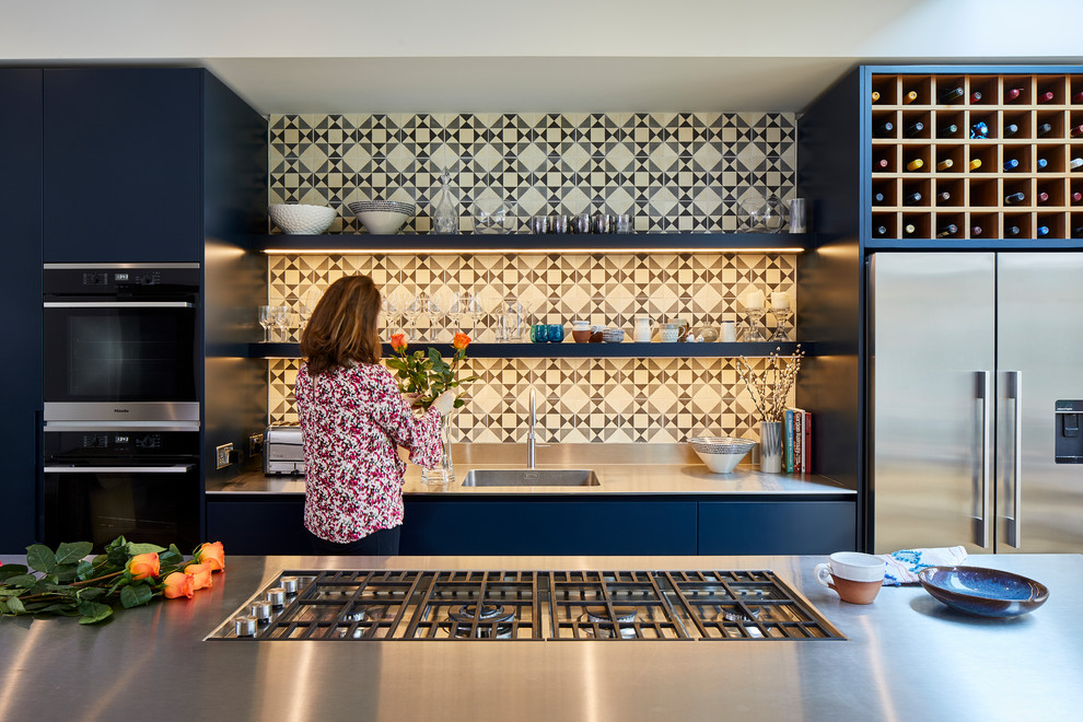 Moderne Küche mit integriertem Waschbecken, flächenbündigen Schrankfronten, blauen Schränken, Edelstahl-Arbeitsplatte, bunter Rückwand, Küchengeräten aus Edelstahl und Kücheninsel in London