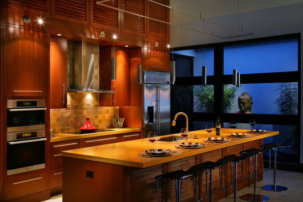 Exempel på ett mellanstort exotiskt kök, med rostfria vitvaror, en undermonterad diskho, släta luckor, skåp i mörkt trä, brunt stänkskydd, stänkskydd i stenkakel och en köksö
