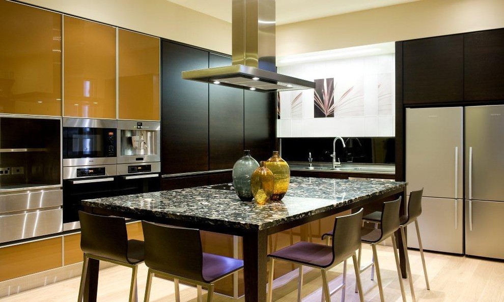 Photo of a contemporary l-shaped kitchen in Auckland with stainless steel appliances, flat-panel cabinets, a double-bowl sink, dark wood cabinets, granite worktops, light hardwood flooring, an island and black splashback.
