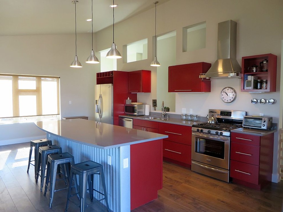 Inspiration for a small industrial single-wall medium tone wood floor open concept kitchen remodel in Denver with an undermount sink, flat-panel cabinets, red cabinets, quartz countertops, gray backsplash, stainless steel appliances and an island