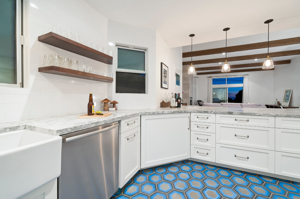 Inspiration for a nautical u-shaped kitchen in San Diego with a belfast sink, white cabinets, granite worktops, white splashback, ceramic splashback, stainless steel appliances and concrete flooring.