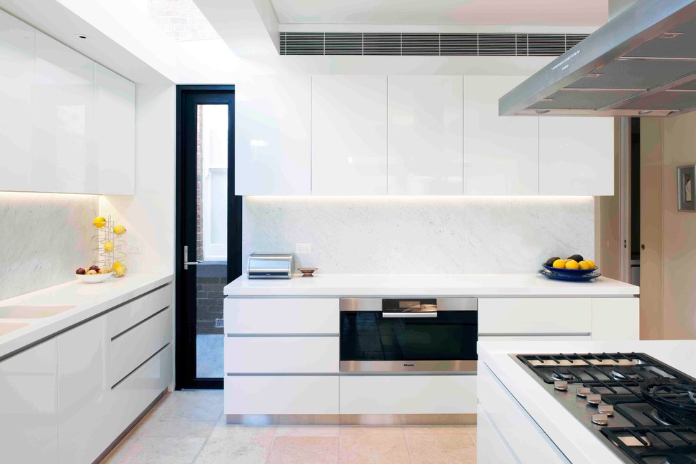 На фото: кухня в современном стиле с плоскими фасадами, белыми фасадами, белым фартуком и островом с