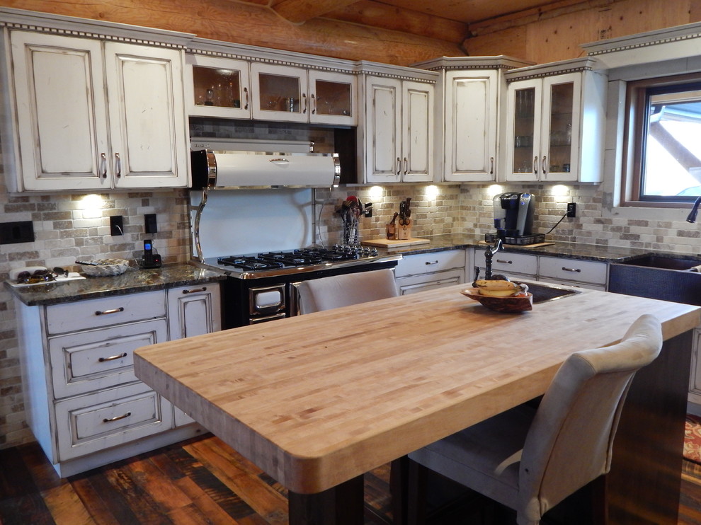 Inspiration for a mid-sized rustic u-shaped dark wood floor kitchen remodel in Vancouver with two islands, raised-panel cabinets, distressed cabinets, wood countertops, beige backsplash, colored appliances and a farmhouse sink