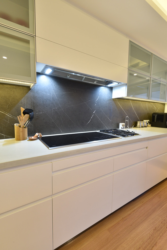 Large modern l-shaped open plan kitchen in Brisbane with a double-bowl sink, porcelain splashback, stainless steel appliances, an island, flat-panel cabinets, white cabinets, black splashback, light hardwood flooring and brown floors.