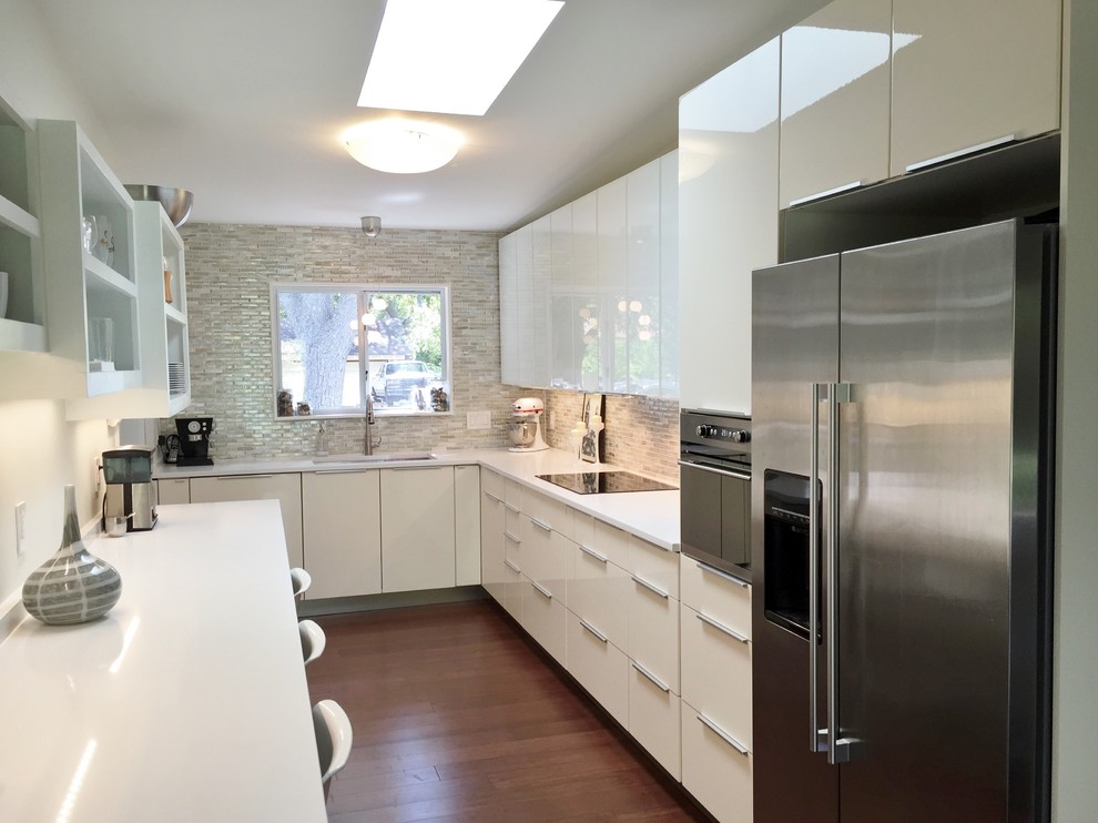 This is an example of a modern galley enclosed kitchen in Austin with a single-bowl sink, flat-panel cabinets, white cabinets, engineered stone countertops, multi-coloured splashback, glass tiled splashback, stainless steel appliances and dark hardwood flooring.