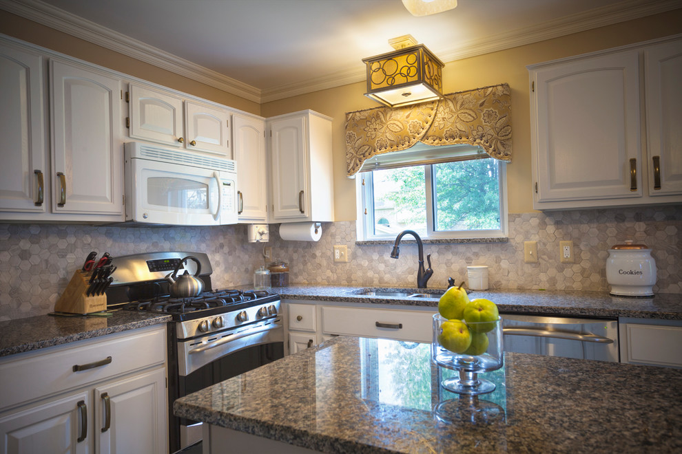 Klassisk inredning av ett mellanstort kök, med en undermonterad diskho, luckor med upphöjd panel, vita skåp, granitbänkskiva, grått stänkskydd, stänkskydd i porslinskakel, vita vitvaror, en köksö och brunt golv