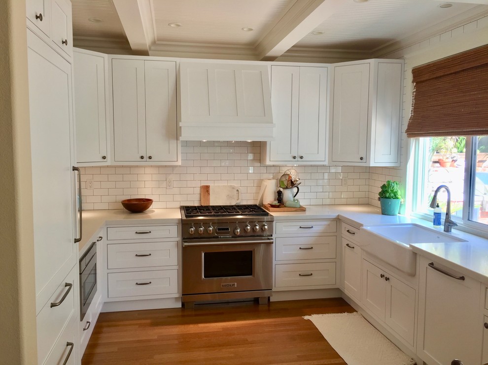 Example of a large beach style u-shaped dark wood floor and brown floor kitchen pantry design in San Diego with a farmhouse sink, beaded inset cabinets, white cabinets, quartz countertops, white backsplash, subway tile backsplash, paneled appliances, no island and white countertops