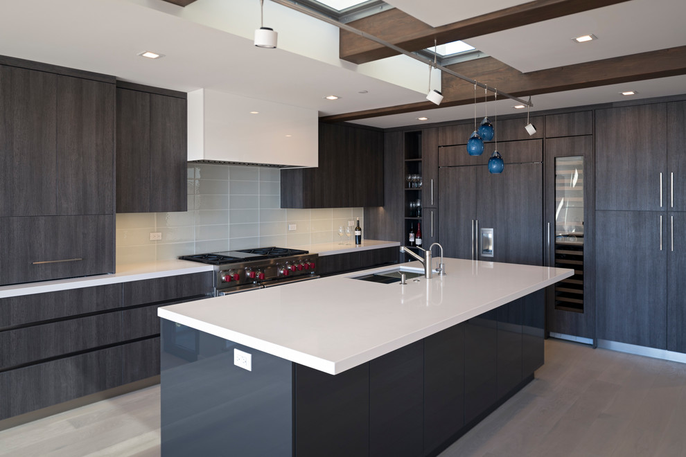 Photo of a large modern l-shaped open plan kitchen in San Diego with a submerged sink, flat-panel cabinets, dark wood cabinets, engineered stone countertops, white splashback, glass tiled splashback, integrated appliances, light hardwood flooring, an island and white worktops.