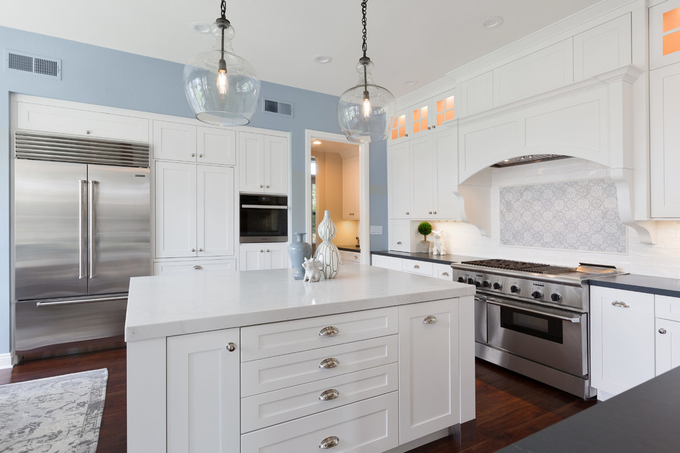 This is an example of a large classic u-shaped kitchen in Tampa with a belfast sink, shaker cabinets, white cabinets, soapstone worktops, white splashback, metro tiled splashback, stainless steel appliances, dark hardwood flooring, an island, brown floors and grey worktops.
