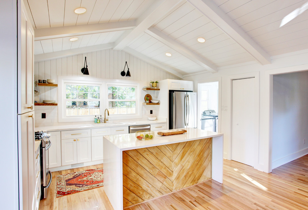 Inspiration for a mid-sized transitional l-shaped light wood floor and brown floor open concept kitchen remodel in Atlanta with an undermount sink, recessed-panel cabinets, white cabinets, quartz countertops, white backsplash, wood backsplash, stainless steel appliances and an island