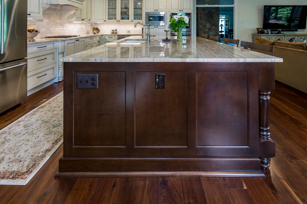 Example of a large classic l-shaped medium tone wood floor and brown floor open concept kitchen design in Charlotte with an undermount sink, flat-panel cabinets, beige cabinets, granite countertops, beige backsplash, travertine backsplash, stainless steel appliances and an island
