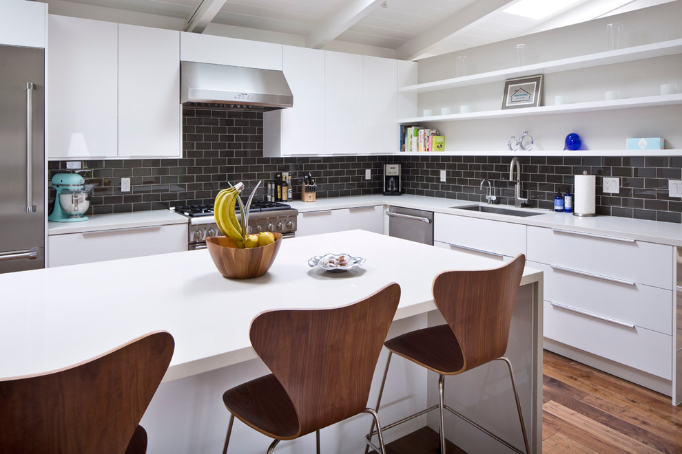 This is an example of a large retro l-shaped kitchen/diner in San Francisco with a submerged sink, flat-panel cabinets, white cabinets, engineered stone countertops, black splashback, metro tiled splashback, stainless steel appliances, dark hardwood flooring and an island.