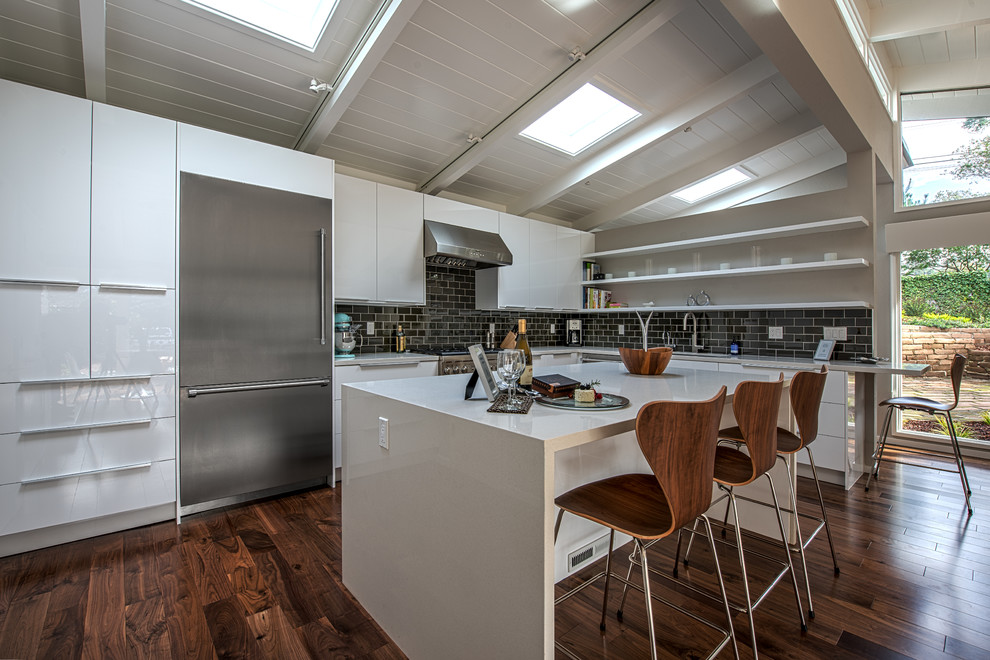 Large contemporary l-shaped kitchen/diner in Other with flat-panel cabinets, white cabinets, engineered stone countertops, black splashback, metro tiled splashback, stainless steel appliances and an island.