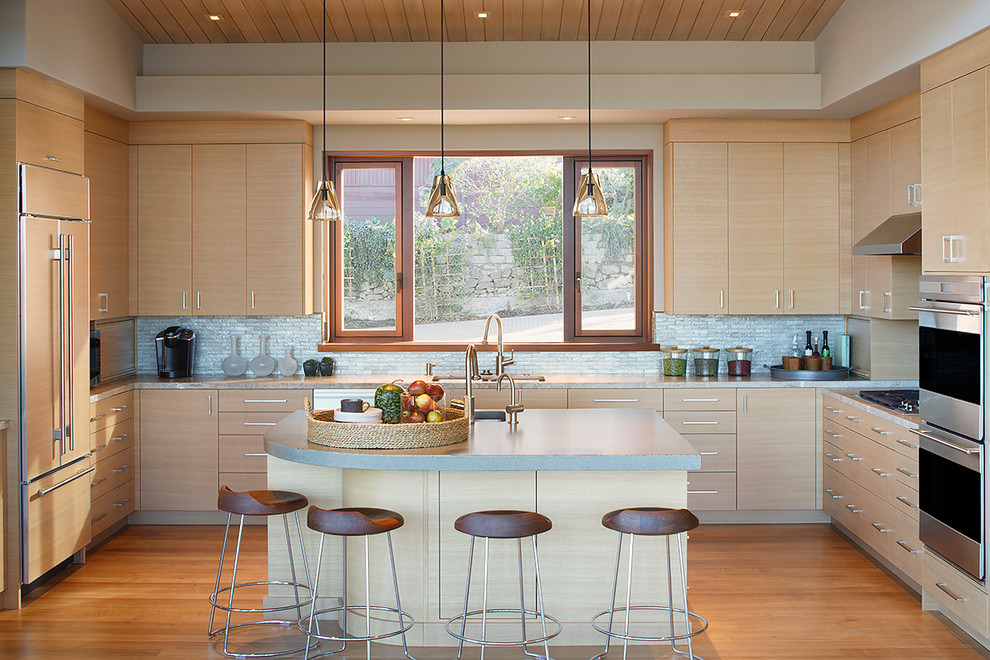 Foto på ett funkis kök, med en undermonterad diskho, släta luckor, skåp i ljust trä, bänkskiva i betong, grått stänkskydd, stänkskydd i glaskakel, rostfria vitvaror, mellanmörkt trägolv och en köksö