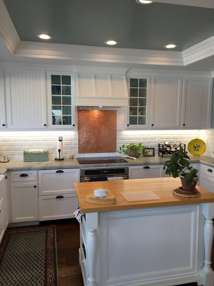 Design ideas for a medium sized farmhouse u-shaped kitchen/diner in San Diego with a belfast sink, beaded cabinets, white cabinets, composite countertops, white splashback, ceramic splashback, stainless steel appliances, dark hardwood flooring and an island.