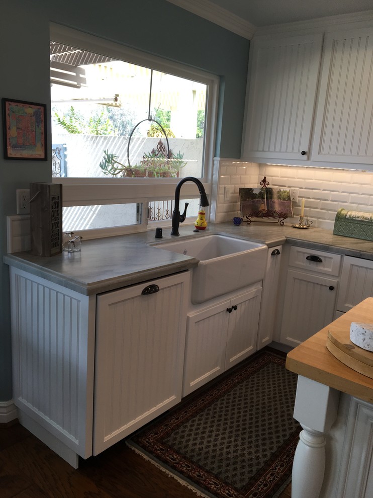 Inspiration for a mid-sized farmhouse u-shaped dark wood floor eat-in kitchen remodel in San Diego with a farmhouse sink, beaded inset cabinets, white cabinets, solid surface countertops, white backsplash, ceramic backsplash, white appliances and an island