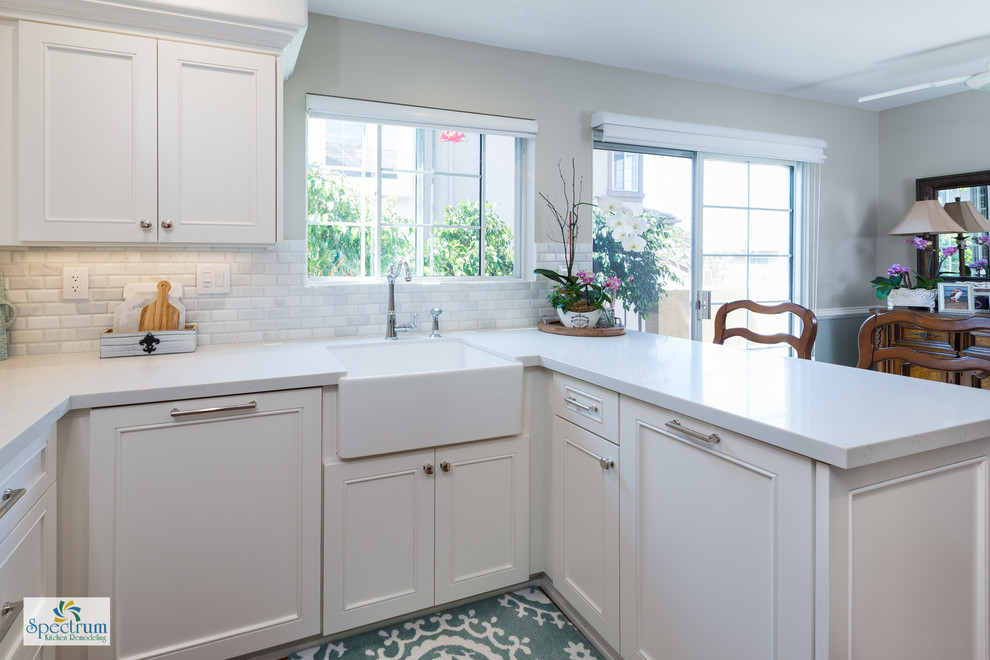 Photo of a small traditional u-shaped kitchen/diner in San Diego with a belfast sink, beaded cabinets, white cabinets, engineered stone countertops, white splashback, metro tiled splashback, stainless steel appliances, dark hardwood flooring and a breakfast bar.