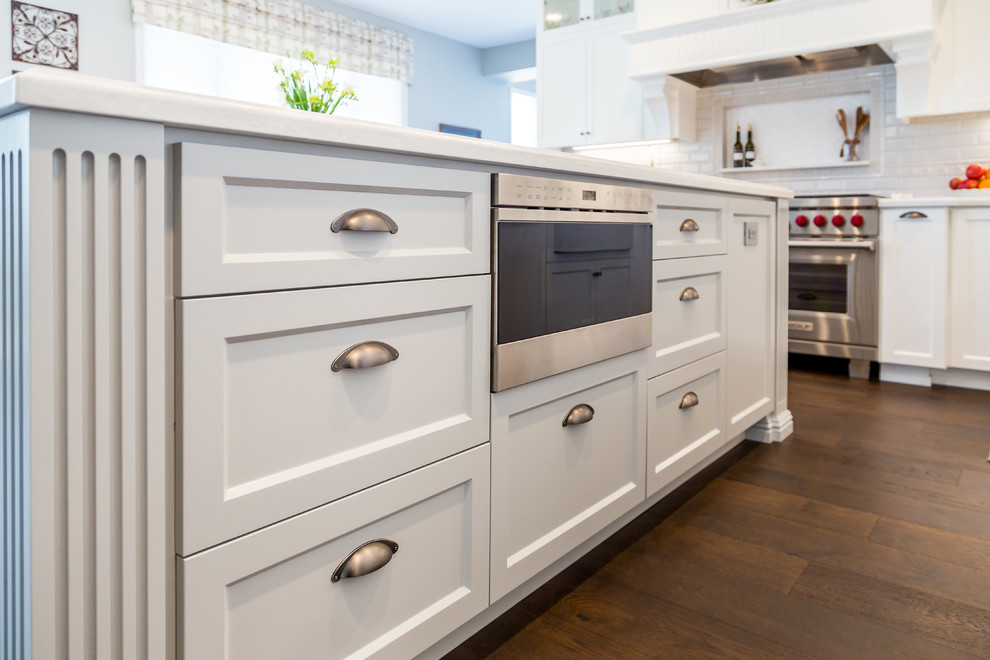 Large traditional l-shaped kitchen/diner in San Diego with a belfast sink, shaker cabinets, white cabinets, marble worktops, white splashback, porcelain splashback, stainless steel appliances, dark hardwood flooring, an island, brown floors and white worktops.