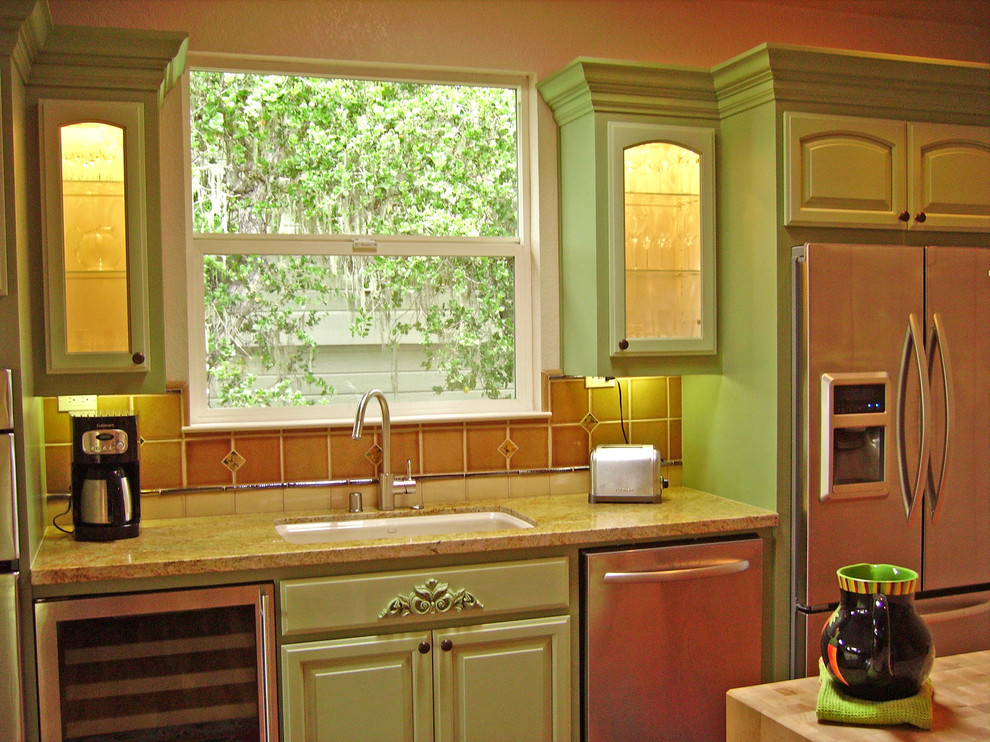 Exempel på ett mellanstort lantligt kök, med en undermonterad diskho, luckor med upphöjd panel, gröna skåp, granitbänkskiva, beige stänkskydd, stänkskydd i keramik, rostfria vitvaror, mellanmörkt trägolv, en köksö och brunt golv