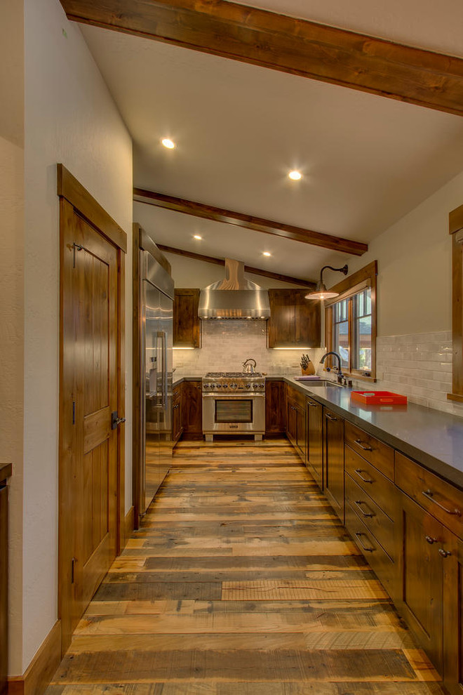 This is an example of a large rustic galley kitchen/diner in Sacramento with a built-in sink, shaker cabinets, medium wood cabinets, quartz worktops, white splashback, porcelain splashback, stainless steel appliances, medium hardwood flooring and no island.