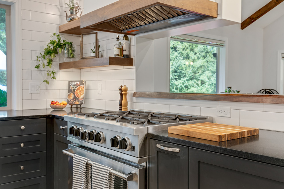 Mid-sized country eat-in kitchen photo in Portland with a farmhouse sink, shaker cabinets, black cabinets, soapstone countertops, white backsplash, subway tile backsplash, stainless steel appliances and black countertops