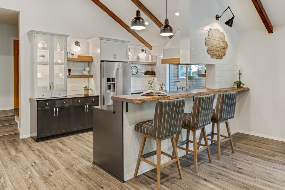 Eat-in kitchen - mid-sized country brown floor eat-in kitchen idea in Portland with a farmhouse sink, shaker cabinets, black cabinets, soapstone countertops, white backsplash, subway tile backsplash, stainless steel appliances and black countertops