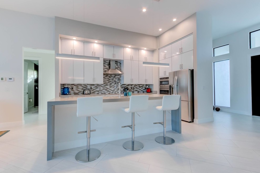 Bild på ett stort funkis grå linjärt grått kök med öppen planlösning, med en rustik diskho, släta luckor, vita skåp, bänkskiva i kvarts, flerfärgad stänkskydd, stänkskydd i glaskakel, rostfria vitvaror, en köksö och vitt golv
