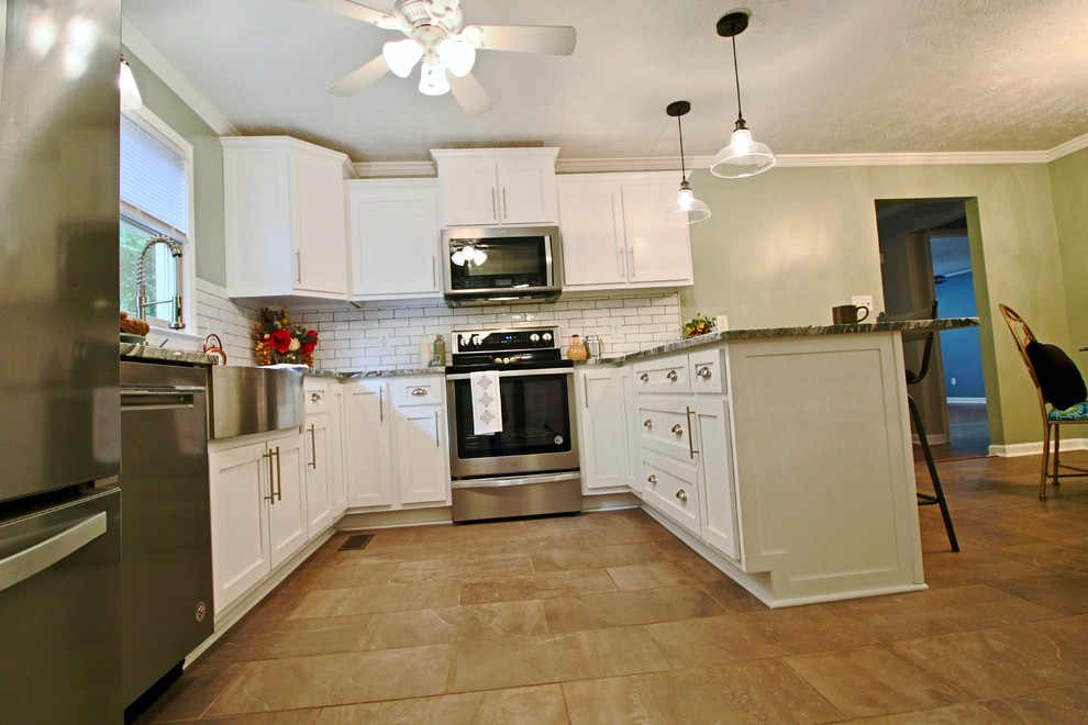 Klassisk inredning av ett mellanstort kök, med en rustik diskho, skåp i shakerstil, vita skåp, granitbänkskiva, vitt stänkskydd, stänkskydd i keramik, rostfria vitvaror, klinkergolv i keramik, en halv köksö och brunt golv