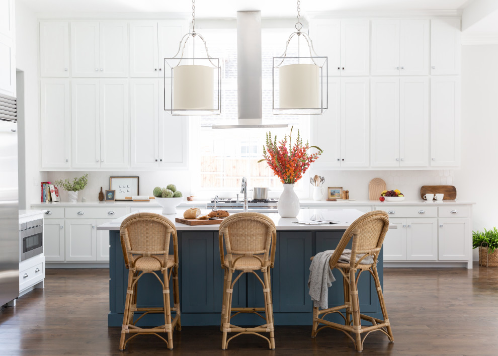 Inspiration for an expansive nautical l-shaped open plan kitchen in Dallas with a submerged sink, shaker cabinets, white cabinets, engineered stone countertops, white splashback, ceramic splashback, stainless steel appliances, dark hardwood flooring, an island, brown floors and white worktops.