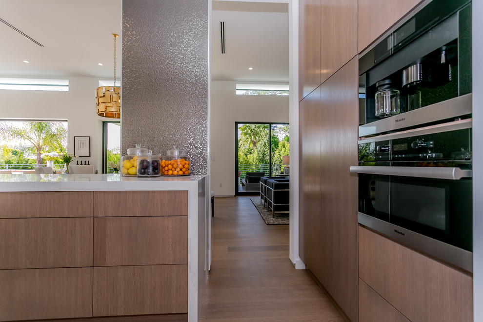 Eat-in kitchen - huge contemporary medium tone wood floor eat-in kitchen idea in Los Angeles with an undermount sink, flat-panel cabinets, medium tone wood cabinets, solid surface countertops, metallic backsplash, porcelain backsplash, stainless steel appliances and an island