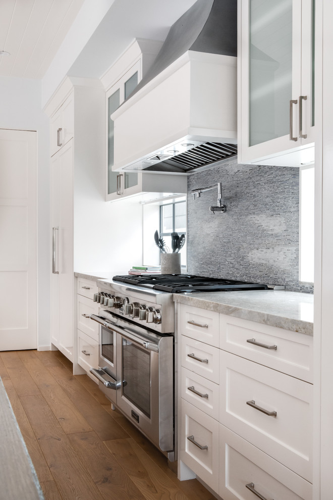 Bild på ett stort funkis grå grått l-kök, med en rustik diskho, luckor med infälld panel, vita skåp, bänkskiva i kvartsit, grått stänkskydd, stänkskydd i sten, integrerade vitvaror, ljust trägolv, en köksö och beiget golv