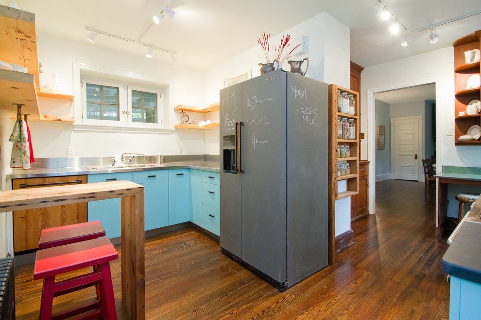 Eklektisk inredning av ett avskilt kök, med en dubbel diskho, släta luckor, blå skåp, bänkskiva i rostfritt stål och integrerade vitvaror
