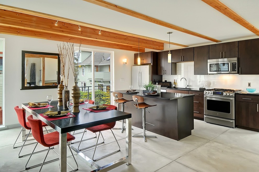 Moderne Wohnküche mit flächenbündigen Schrankfronten, dunklen Holzschränken, Küchenrückwand in Weiß, Küchengeräten aus Edelstahl, Betonboden und Kücheninsel in Seattle