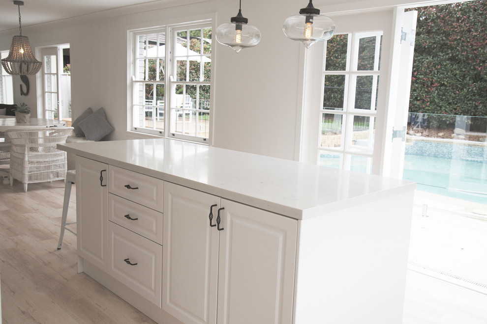 Example of a trendy l-shaped plywood floor open concept kitchen design in Sydney with quartz countertops, an undermount sink, raised-panel cabinets, white cabinets, white backsplash, porcelain backsplash, stainless steel appliances and an island
